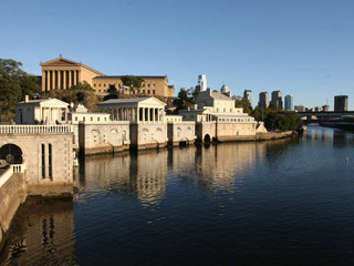 a photograph showing a canal lined with Greek revival style buildings, and showing the Philadelphia skyline in the background. a photograph showing a canal lined with Greek revival style buildings, and showing the Philadelphia skyline in the background.