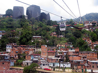 Photo of an informal settlement in Medellin, Colombia with a public library in the background and aerial cable cars above. Photo of an informal settlement in Medellin, Colombia with a public library in the background and aerial cable cars above.
