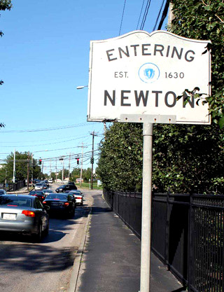 A photograph of cars on a street next to a sign that says "Entering Newton." A photograph of cars on a street next to a sign that says "Entering Newton."