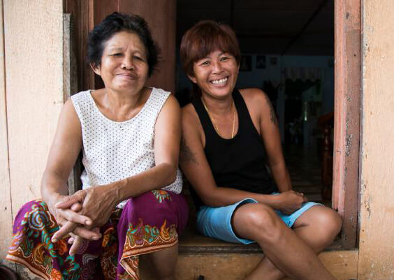 Two smiling women sit close together in a doorway.