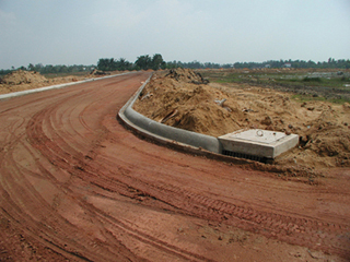 A photograph of a new road being constructed in Vietnam. The photograph shows a recently graded dirt surface as well as curbs and and a drainage system. A photograph of a new road being constructed in Vietnam. The photograph shows a recently graded dirt surface as well as curbs and and a drainage system.