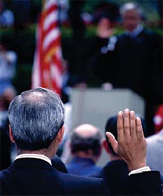 A photo behind a man raising his right hand during a naturalization ceremony. A photo behind a man raising his right hand during a naturalization ceremony.