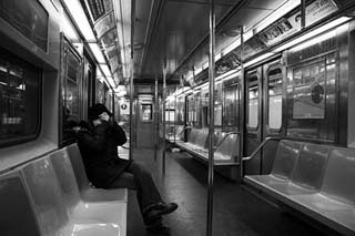 Black and white photograph of one rider on a mostly empty subway. Black and white photograph of one rider on a mostly empty subway.