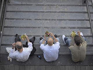 A photograph of three men sitting together on a staircase, eating salads. A photograph of three men sitting together on a staircase, eating salads.