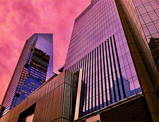 Two glass buildings rise into the sky. They glow pink as they reflect the sunset. Two glass buildings rise into the sky. They glow pink as they reflect the sunset.