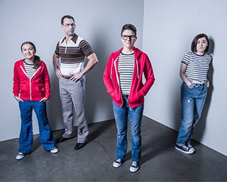 A man with a stern expression stands amongst three females: a preteen, a teenager, and an adult. Each female wears jeans, sneakers, and a striped shirt. A man with a stern expression stands amongst three females: a preteen, a teenager, and an adult. Each female wears jeans, sneakers, and a striped shirt.