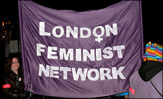 A woman holds a huge purple banner with the words London Feminist Network written on it. A woman holds a huge purple banner with the words London Feminist Network written on it.