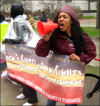 A woman shouts through a megaphone while holding a banner that says "Women's Rights=Human Rights." A woman shouts through a megaphone while holding a banner that says "Women's Rights=Human Rights."