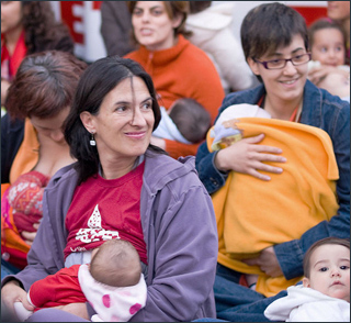 A photograph of a group of women sit on the ground nursing their babies. A photograph of a group of women sit on the ground nursing their babies.