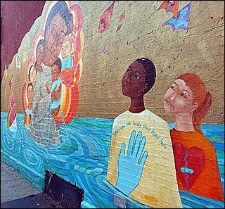 A photographA mural painted on a wall features a body of water in which an African-American boy and a Caucasian girl stand. The image of a woman surrounded by children is next to them. of a pregnant woman, in a blue shirt, holds her belly. A photographA mural painted on a wall features a body of water in which an African-American boy and a Caucasian girl stand. The image of a woman surrounded by children is next to them. of a pregnant woman, in a blue shirt, holds her belly.
