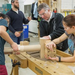 A professor and two students work on assembling the large wooden parts of printing press based on early modern European designs in course 21H.343J.
