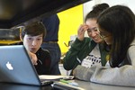 A photo of a workshop volunteer helping a group of girls working at a laptop.