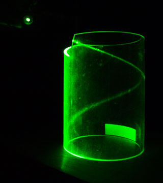 A photograph of green laser light hitting the edge of a transparent cylinder and then curling into a helix due to total internal reflection. A photograph of green laser light hitting the edge of a transparent cylinder and then curling into a helix due to total internal reflection.