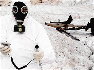 A photograph of a person wearing a hazmat suit and holding a radiation detector, and standing in front of a banner landscape with a destroyed object in the background. A photograph of a person wearing a hazmat suit and holding a radiation detector, and standing in front of a banner landscape with a destroyed object in the background.